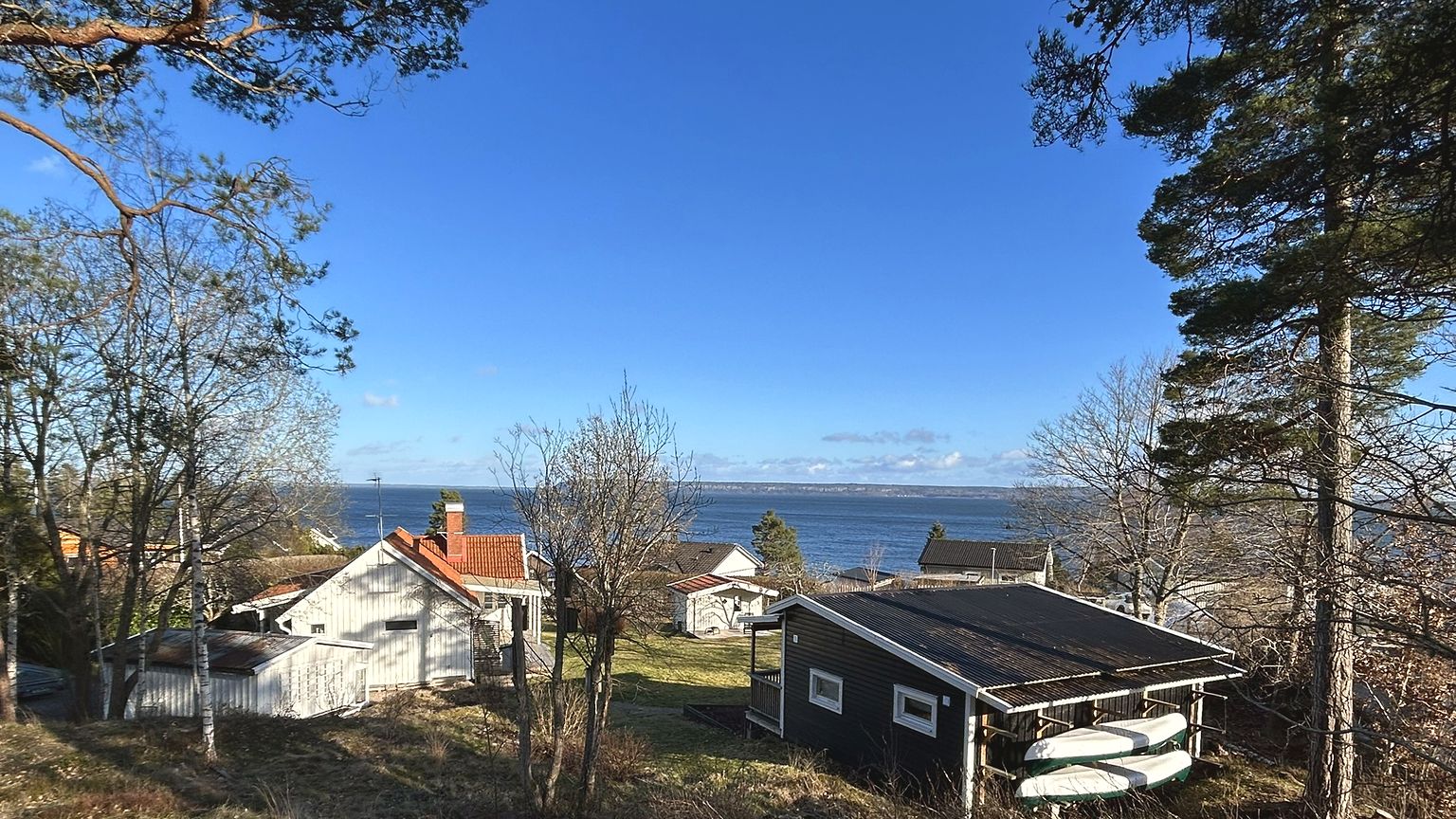 Blick über das Grundstück Solglimten: links das weiße Haupthaus mit rotem Ziegeldach, rechts das schwarze Gästehaus mit gestapelten Kanus, dahinter der Vänernsee.