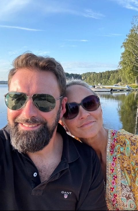 Sabine och Oliver Bartl med solglasögon vid Vänerns strand, i bakgrunden en båtbrygga och skog.