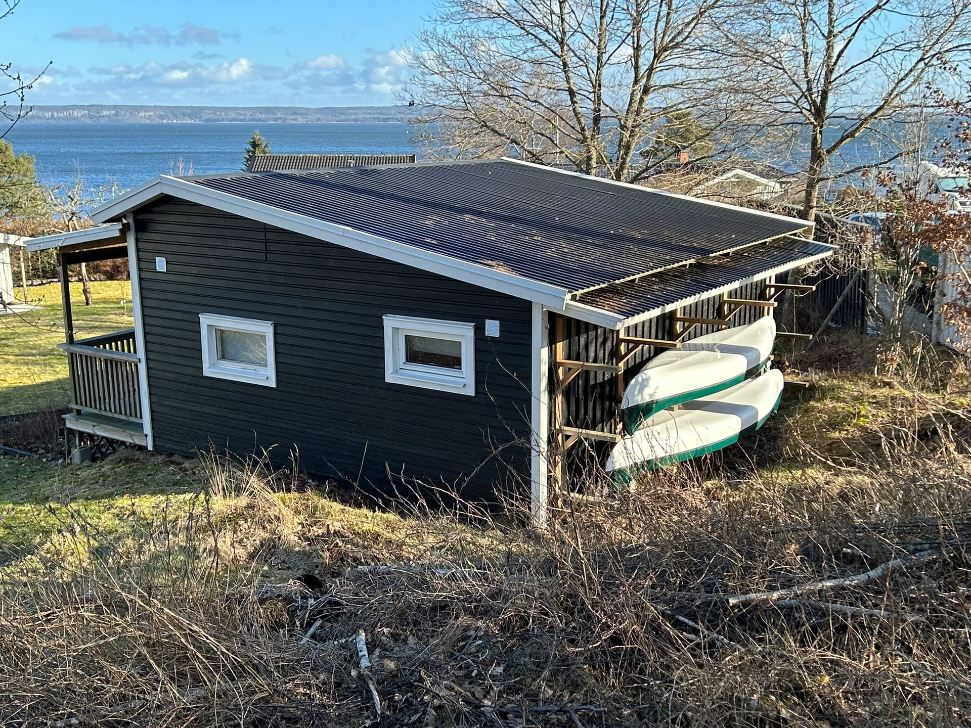 Das schwarze Gästehaus Skogsstugan am Waldrand mit gelagerten Kanus, im Hintergrund der Vänernsee.
