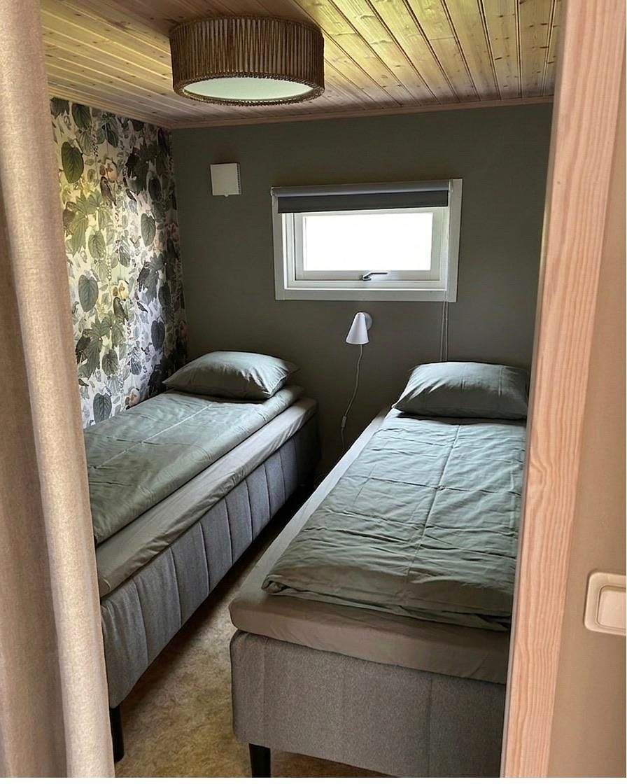 Zwei Einzelbetten mit grüner Bettwäsche, an einer Wand Blumentapete, darüber eine Rattanleuchte.