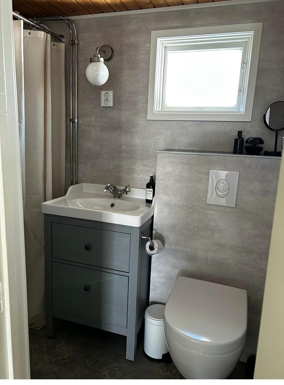 Bad mit grauer Wandverkleidung, grau-blauem Waschtisch, Dusche mit Leinenvorhang und WC.