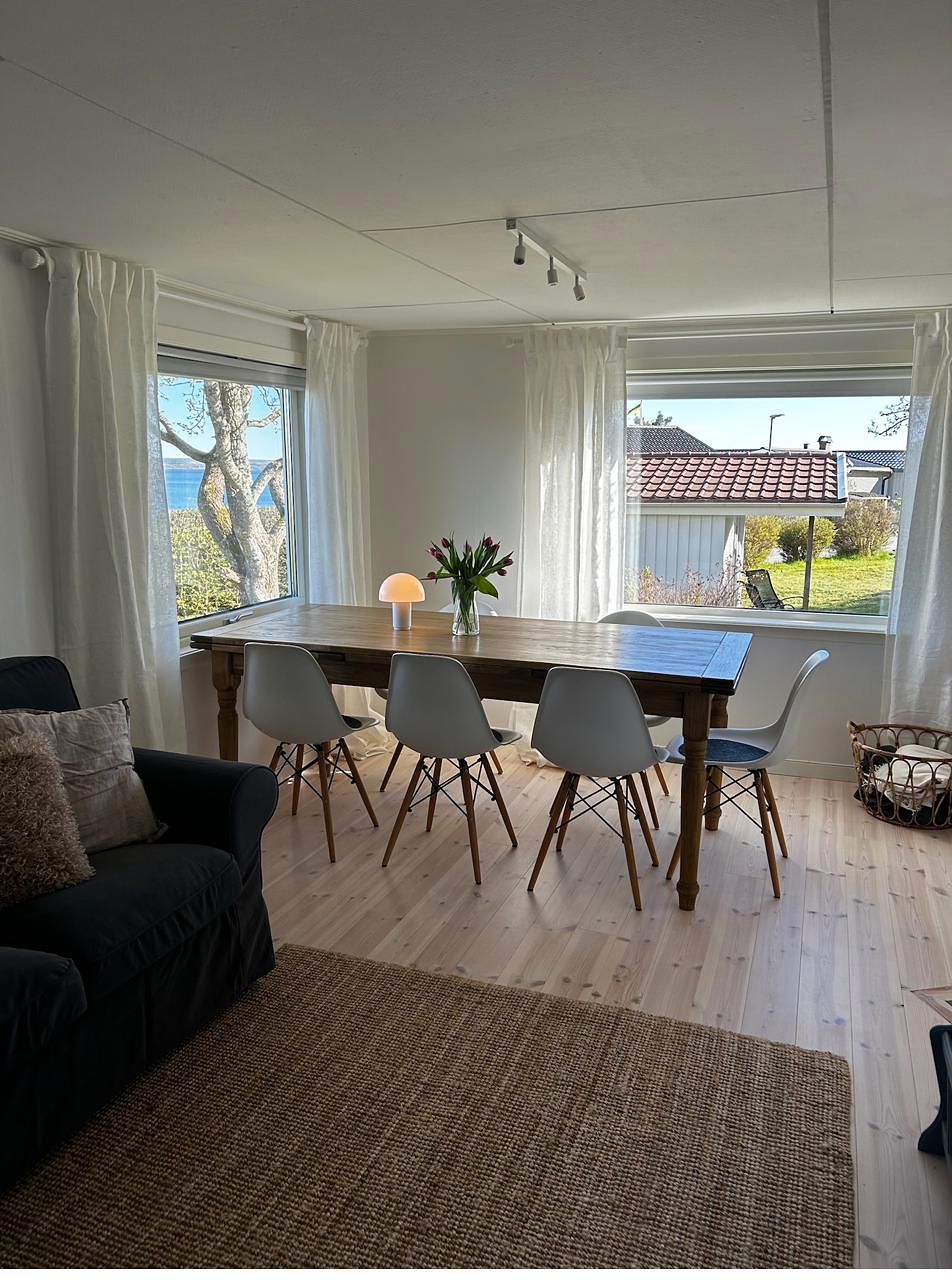 Langer Holztisch mit weißen Schalenstühlen vor zwei Fenstern mit Blick auf den Vänernsee.