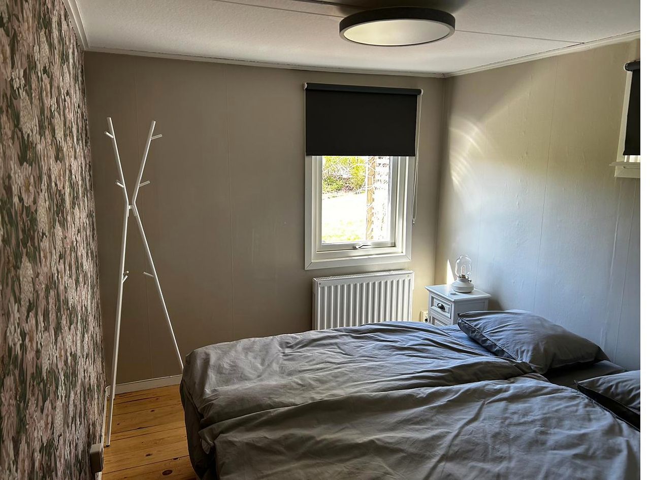 Schlafzimmer mit bezogenem Doppelbett, Blumentapete an einer Wand und Heizkörper unter dem Fenster.