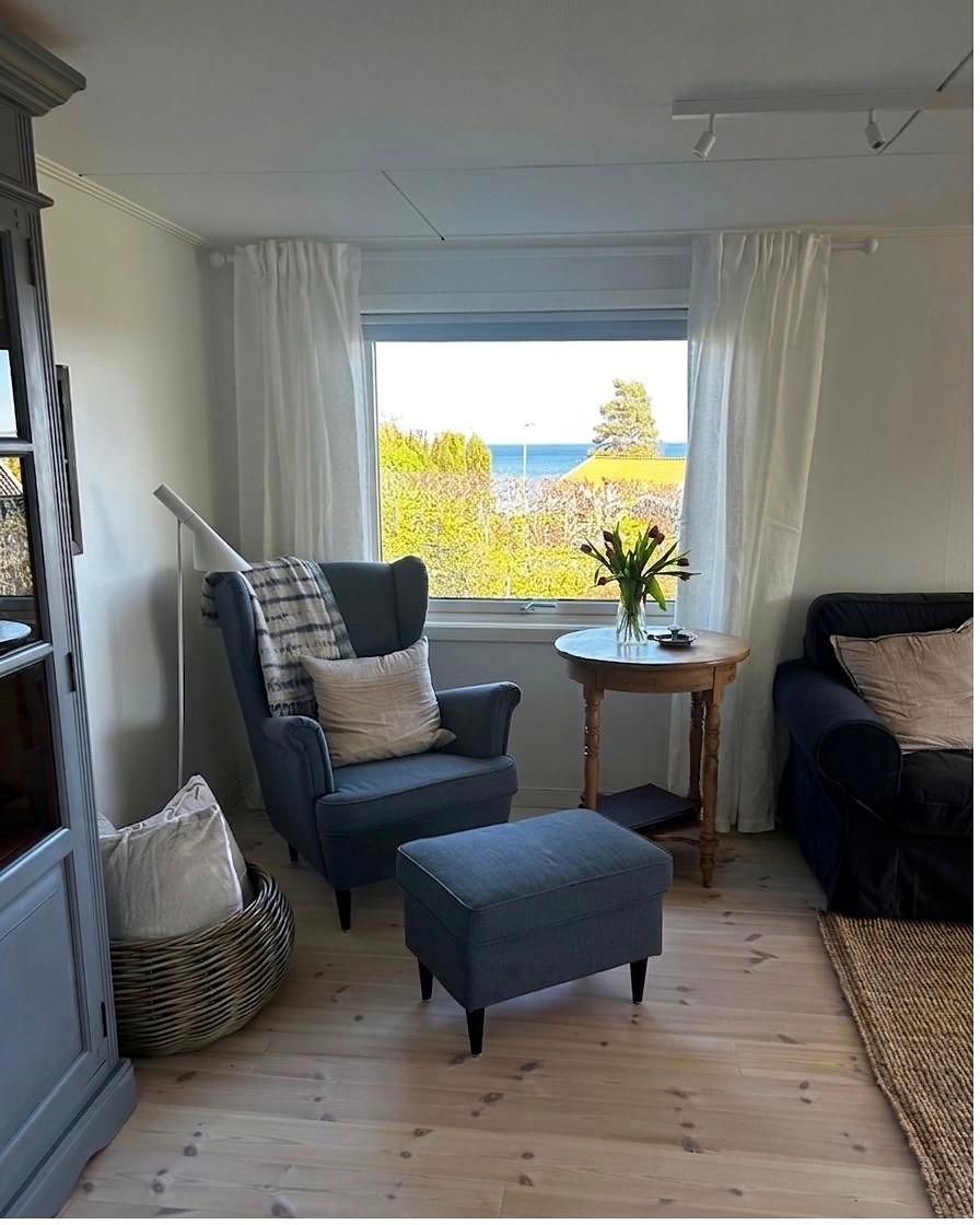 Blauer Ohrensessel mit Fußhocker am Fenster, davor ein runder Beistelltisch mit Tulpen.